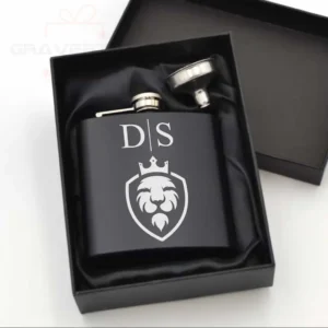 Juoda matinė gertuvė (fleškutė) su išgraviruotu liūto karaliaus logotipu ir inicialais D|S, pateikta prabangioje juodoje dovanų dėžutėje su piltuvėliu