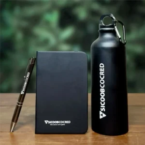 Ekonomiškas verslo dovanų rinkinis: juoda užrašų knygutė, rašiklis ir gertuvė su graviruotu logotipu ant medinio stalo.