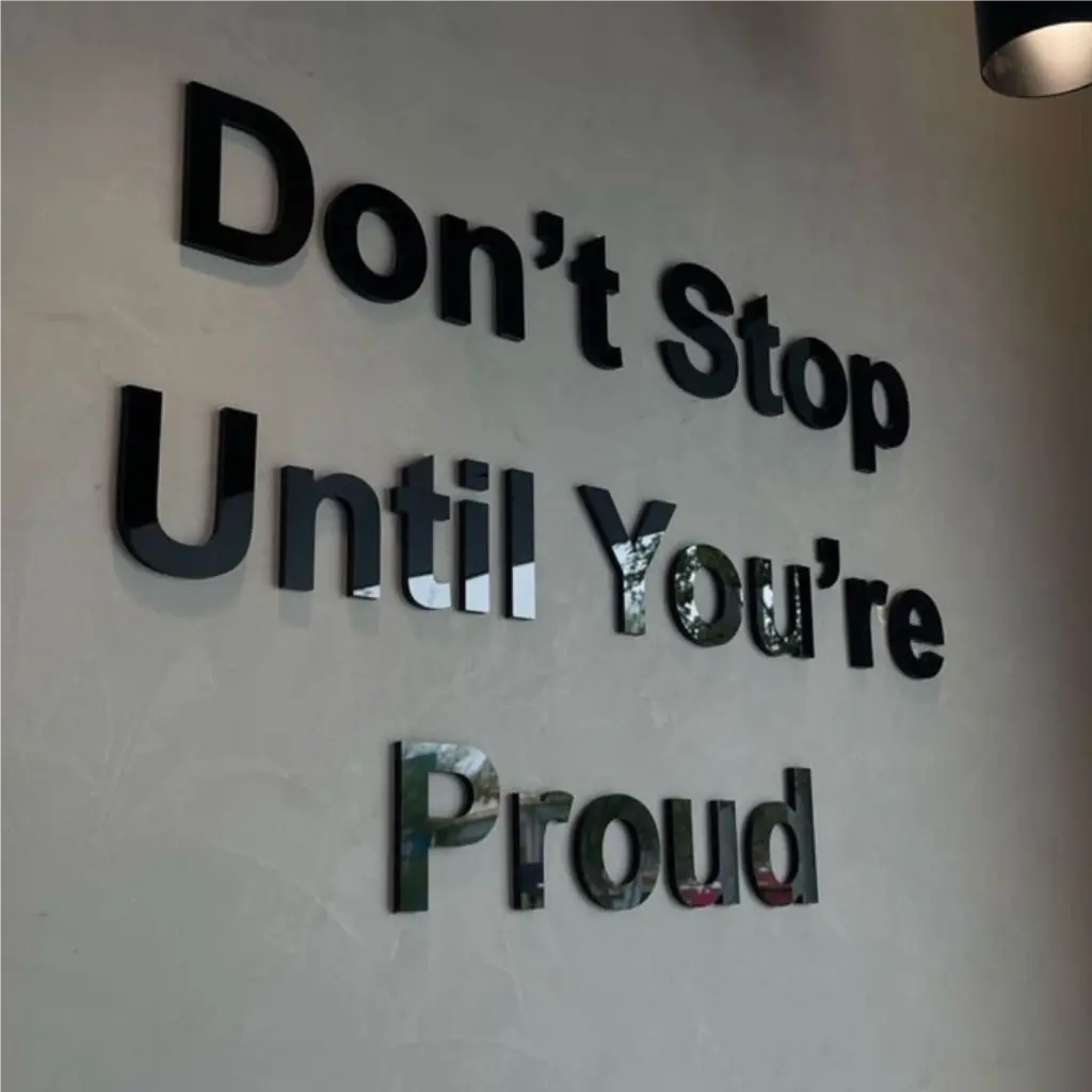 Lazeriu pjautos juodo blizgaus organinio stiklo 3D raidės su stipriu klijų sluoksniu, formuojančios motyvacinį užrašą ant sienos verslo interjere.