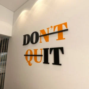 Modernus sienų dekoras su 3D tūrinėmis raidėmis ir lipduku, citata „DON'T DO IT“ juodos ir oranžinės spalvos fone virš darbo vietos.