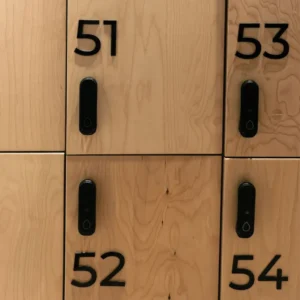 Iškili 3D spintelių numeracija: lazeriu pjauti juodo matinio akrilo skaičiai, sumontuoti ant medinių persirengimo kambario durelių su išmaniosiomis spynomis.