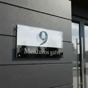 Dviejų dalių (balto ir juodo akrilo) moderni namo numerio lentelė „9 Melduvos gatvė“, pritvirtinta prie tamsaus fasado.