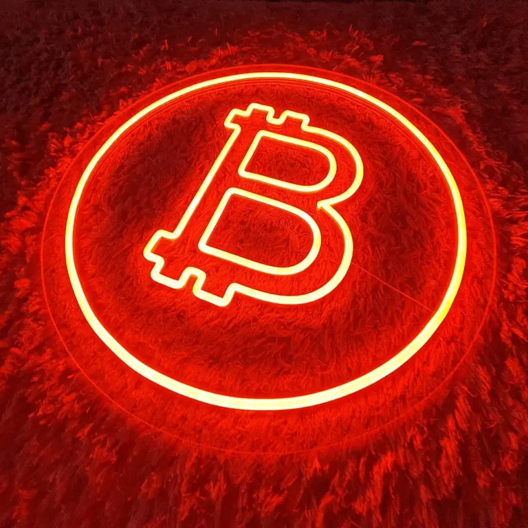 Šviečiantis oranžinis Bitcoin LED neoninis ženklas ant minkšto tamsaus paviršiaus – moderni interjero dekoracija.