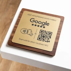 Išmanioji informacinė lentelė „Google“ atsiliepimams rinkti: auksinio metalo plokštelė ant medinio pagrindo su integruotu NFC lustu ir QR kodu greitam skenavimui.
