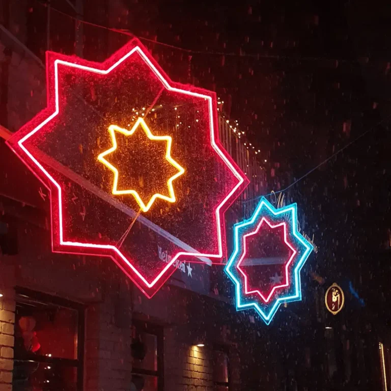Šviečiančios raudonos ir mėlynos LED neono žvaigždės, naudojamos kaip stilinga langų ir pastato fasado dekoracija naktį.
