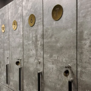 Prabangūs apvalūs auksinio veidrodinio organinio stiklo skaičiai spintelių numeracijai, priklijuoti ant pilkų betoninių durelių, skirti stilingam persirengimo kambarių ir daiktų saugyklų ženklinimui.