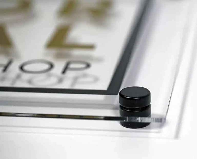 Iš arti nufotografuotas juodas matinis distancinis laikiklis, prilaikantis skaidraus akrilo lentelę